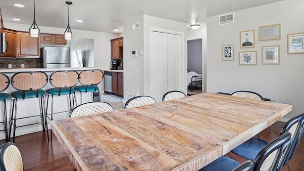 Un comedor con mesa y sillas de madera, una cocina con muebles de madera y electrodomésticos de acero inoxidable, y un pasillo con una puerta blanca.