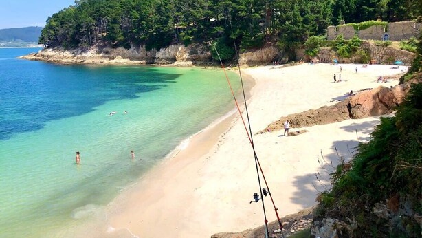 A beach with clear turquoise water, a sandy shore, and a forested hill in the background. - The Cliffs - Piccola Home (Ortigueira)