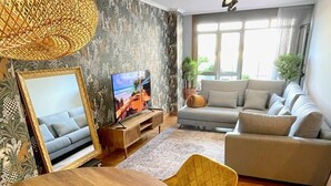A modern living room with a round wooden dining table, a sofa, a TV, and a large window. - The Cliffs - Piccola Home (Ortigueira)