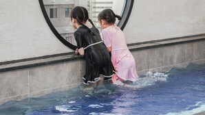 A view through a circular window of a swimming pool area with a building in the background. - Cloudin Hotel Mokpo Peace Square branch (Mokpo)