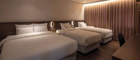 A hotel room with two large beds, a wooden headboard, a desk, and a large window with curtains.