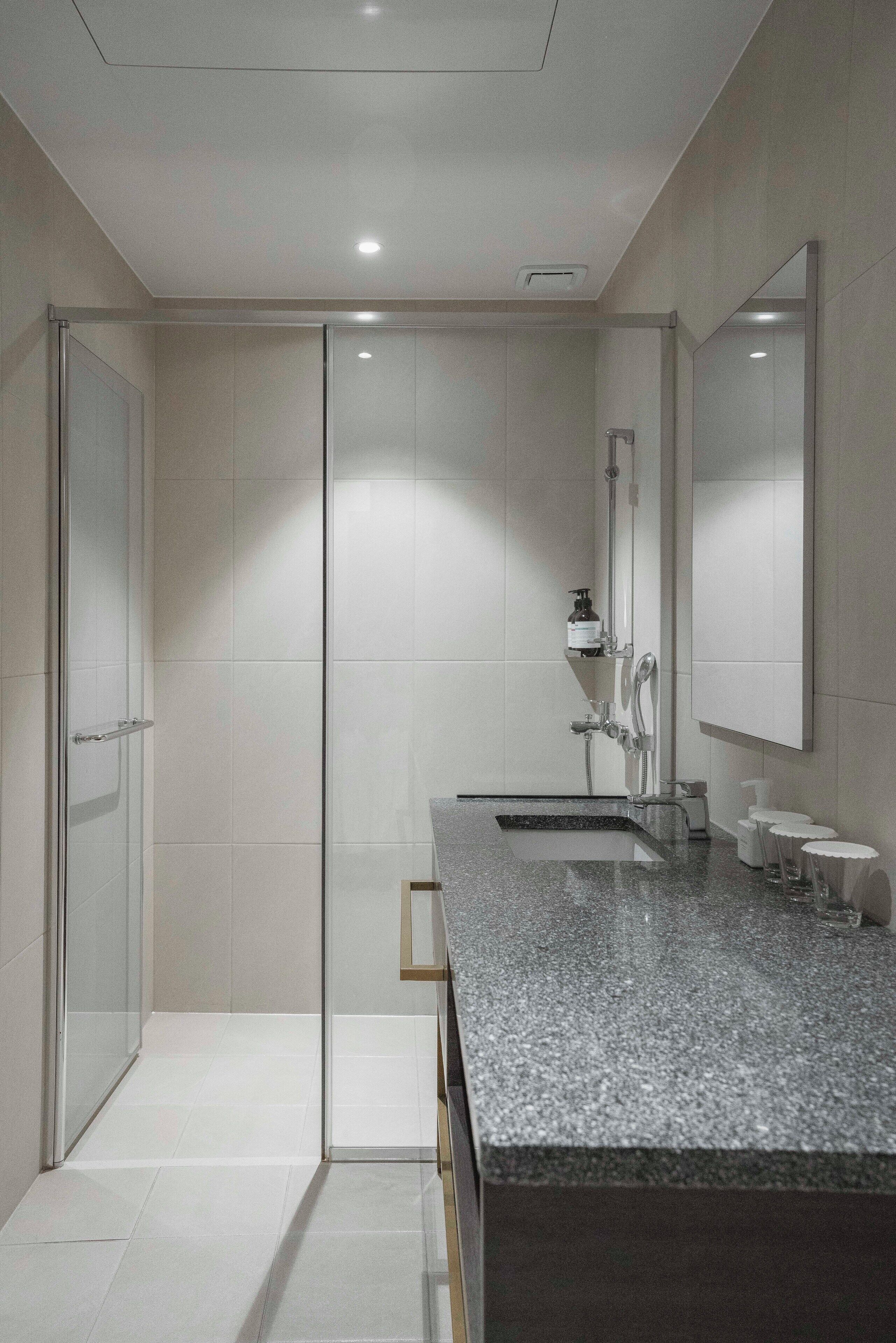 A modern bathroom with a glass shower enclosure, a granite countertop, and a large mirror.