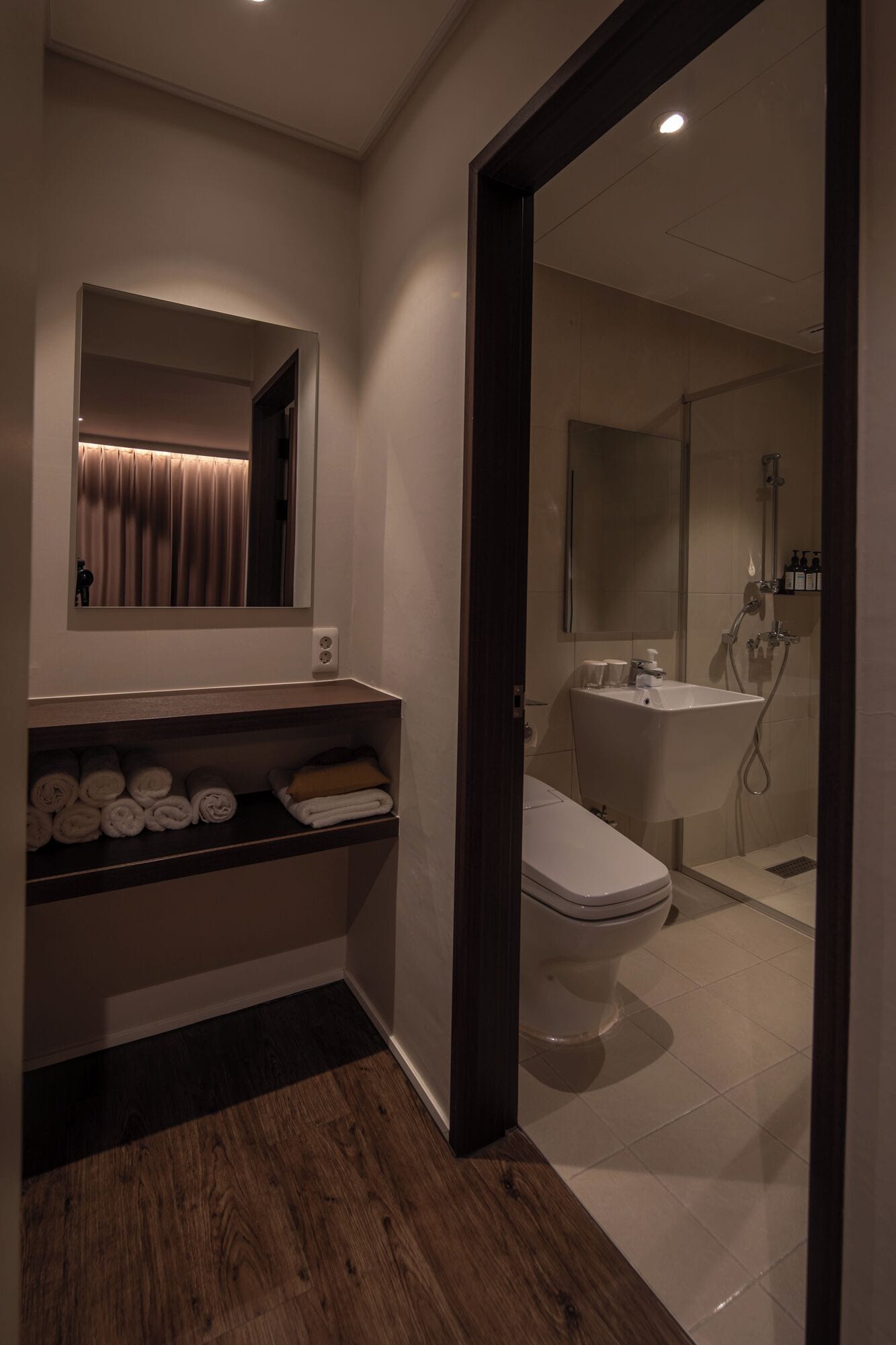 Un baño moderno con inodoro, lavamanos y ducha. Hay un perchero con toallas y un espejo sobre el lavamanos.