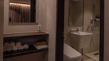 Un baño moderno con inodoro, lavamanos y ducha. Hay un perchero con toallas y un espejo sobre el lavamanos.