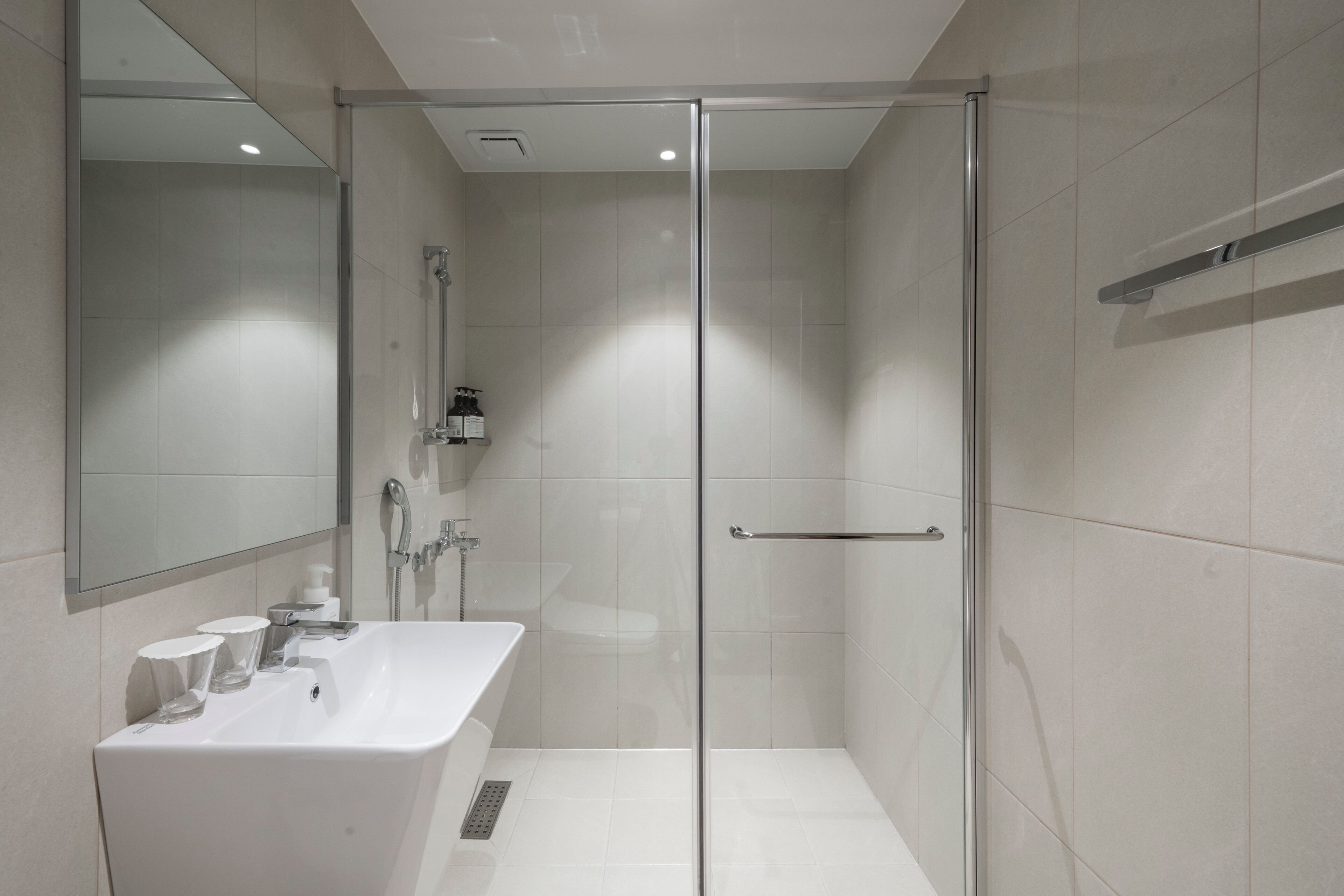 Une salle de bain moderne avec une douche à parois de verre, un lavabo blanc agrémenté d’articles de toilette et un miroir au-dessus du lavabo.