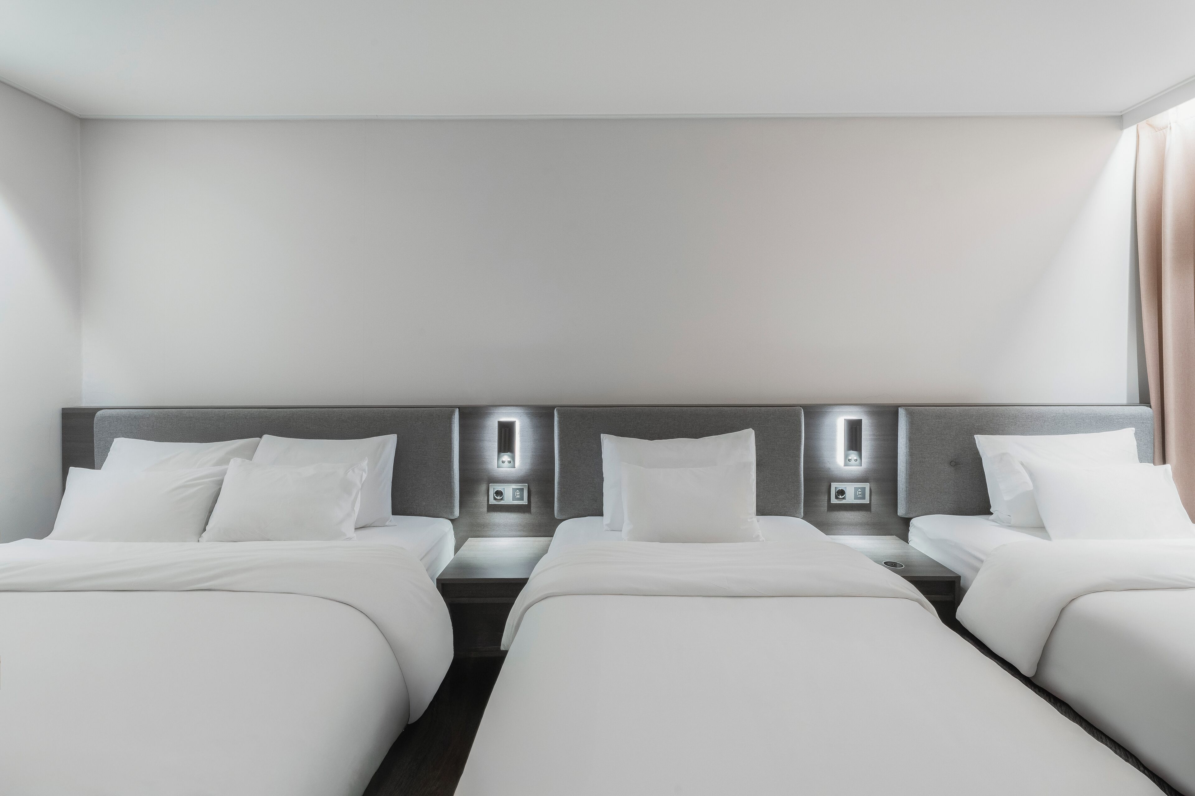 A hotel room with two single beds, each with a headboard, bedside tables, and wall-mounted lighting.