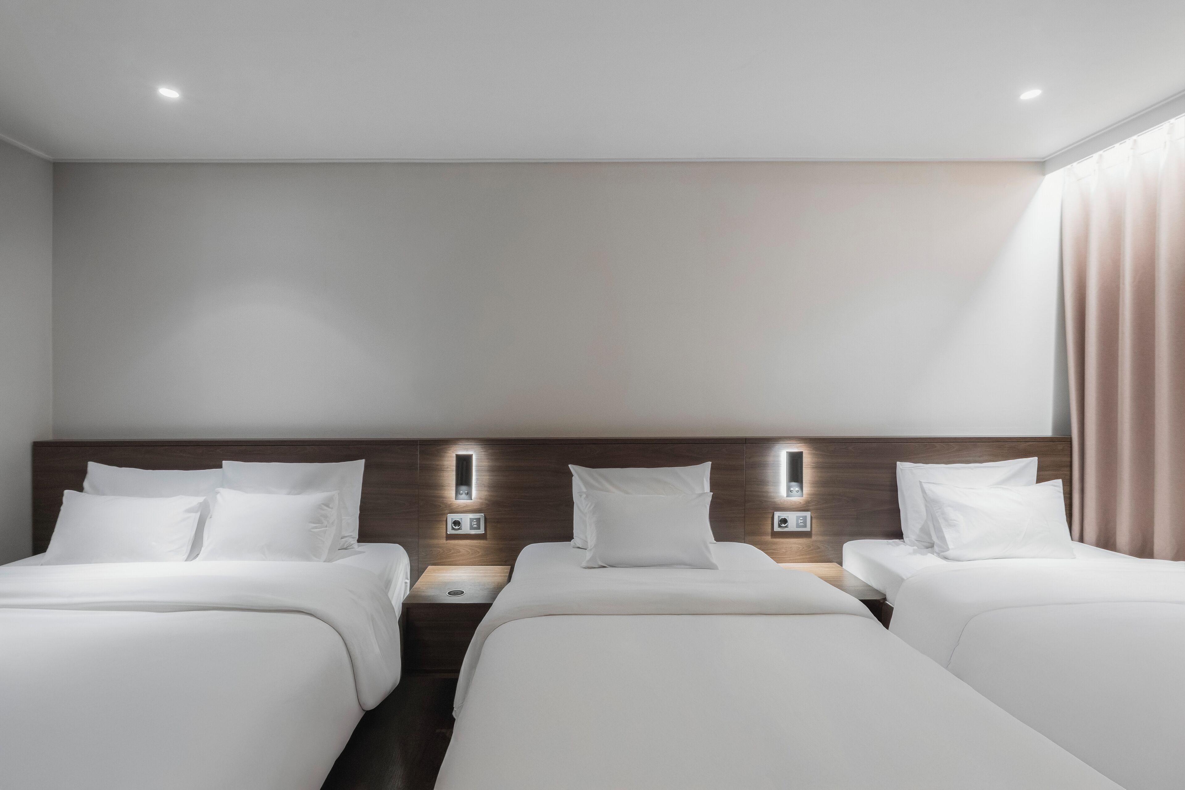 A hotel room with two beds, a wooden headboard, bedside tables with lamps, and a neutral color scheme.