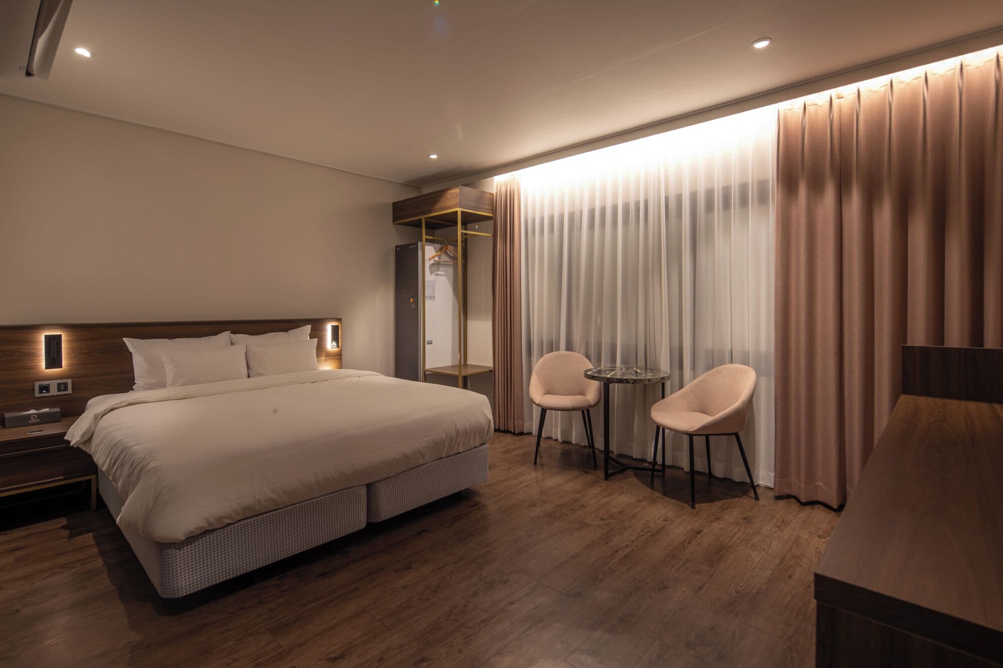 Una habitación de hotel moderna con una cama grande, dos sillones, una mesita, un espejo y un armario.