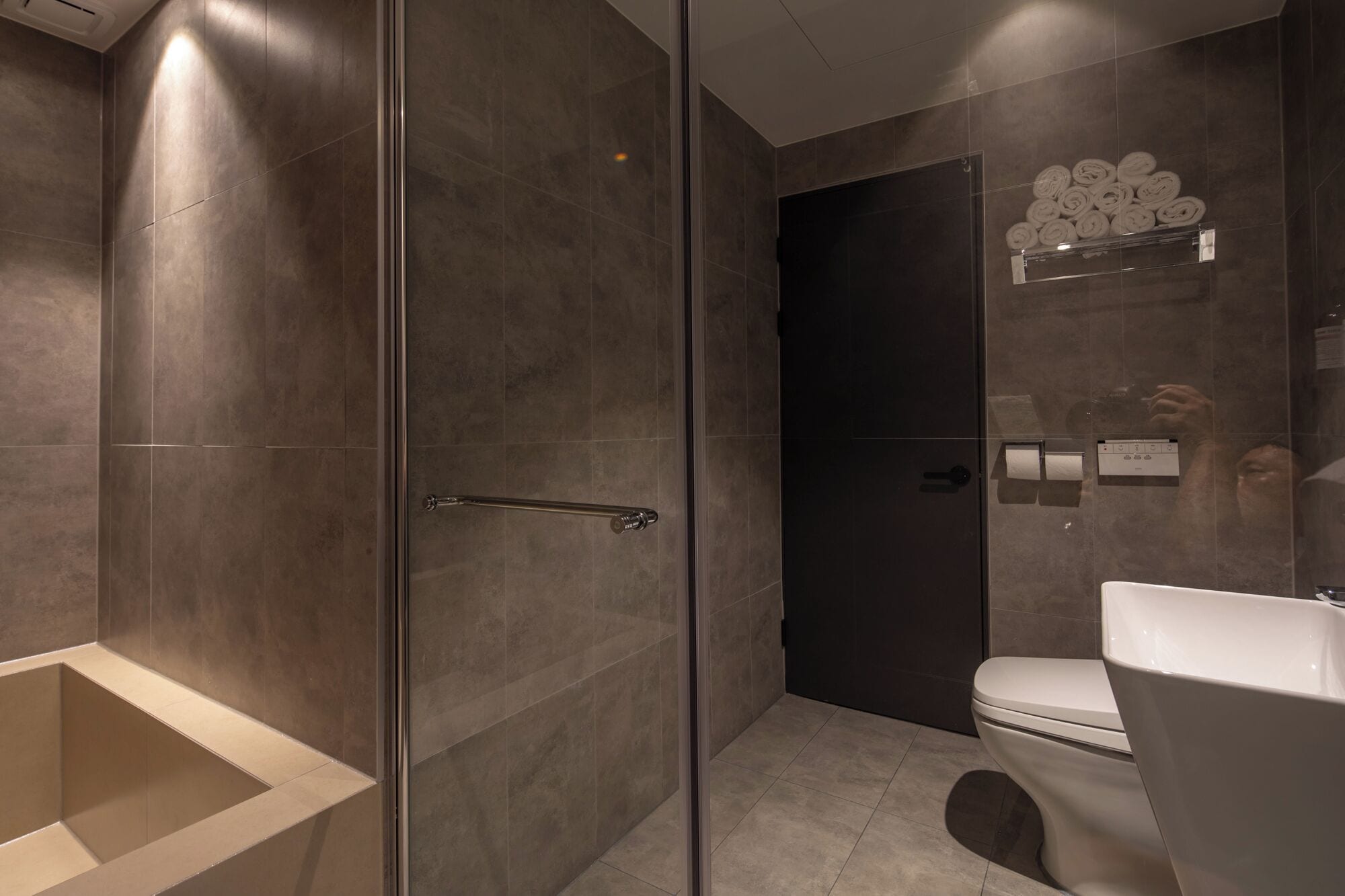 A modern bathroom with a glass shower enclosure, a white toilet, and a towel rack with neatly rolled towels.