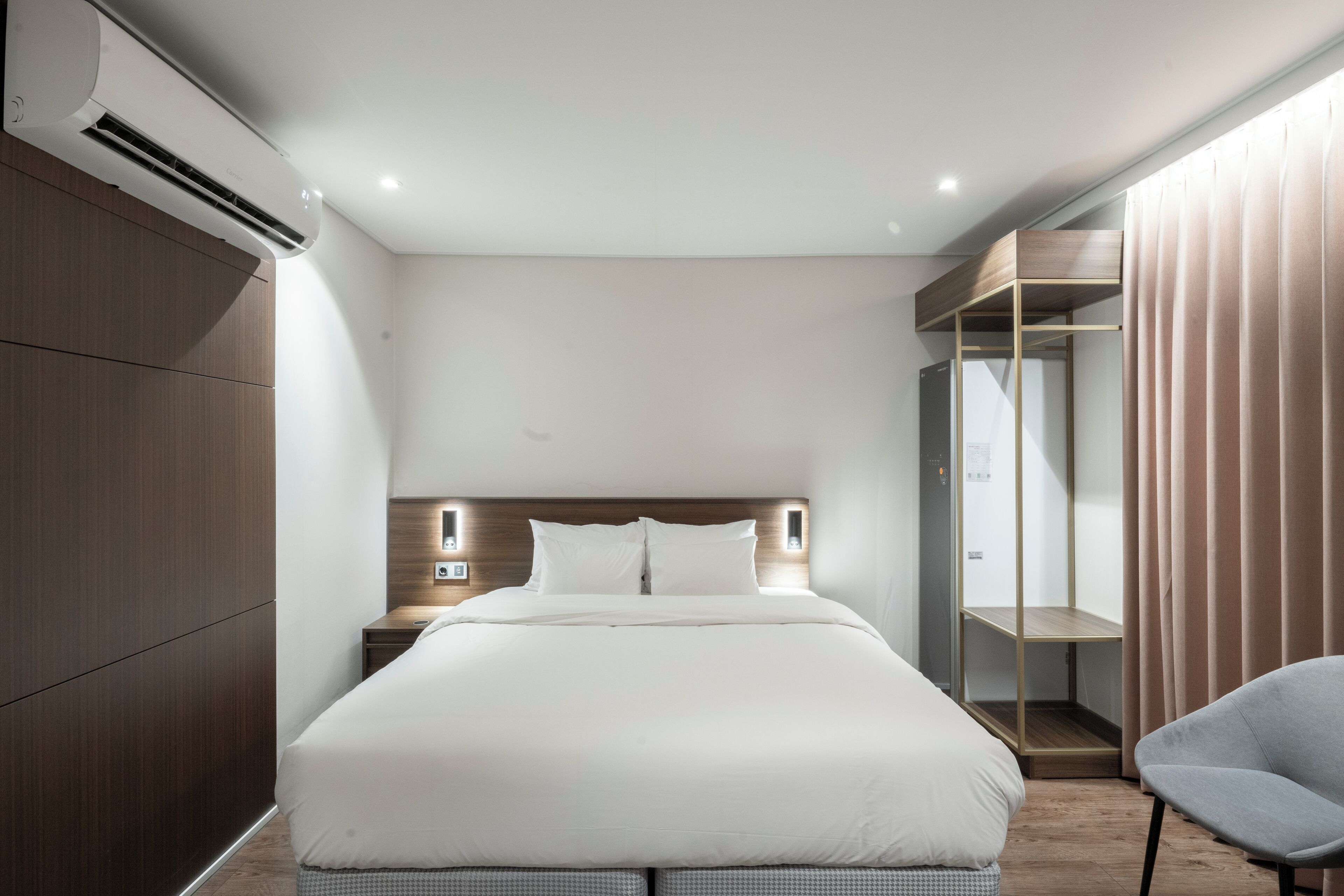 A modern hotel room with a large bed, a wardrobe, a seating area, and a built-in wardrobe with a mirror.