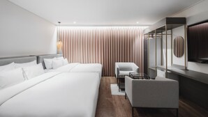 Una habitación de hotel moderna con dos camas, una zona de estar, un televisor y un amplio ventanal con cortinas.