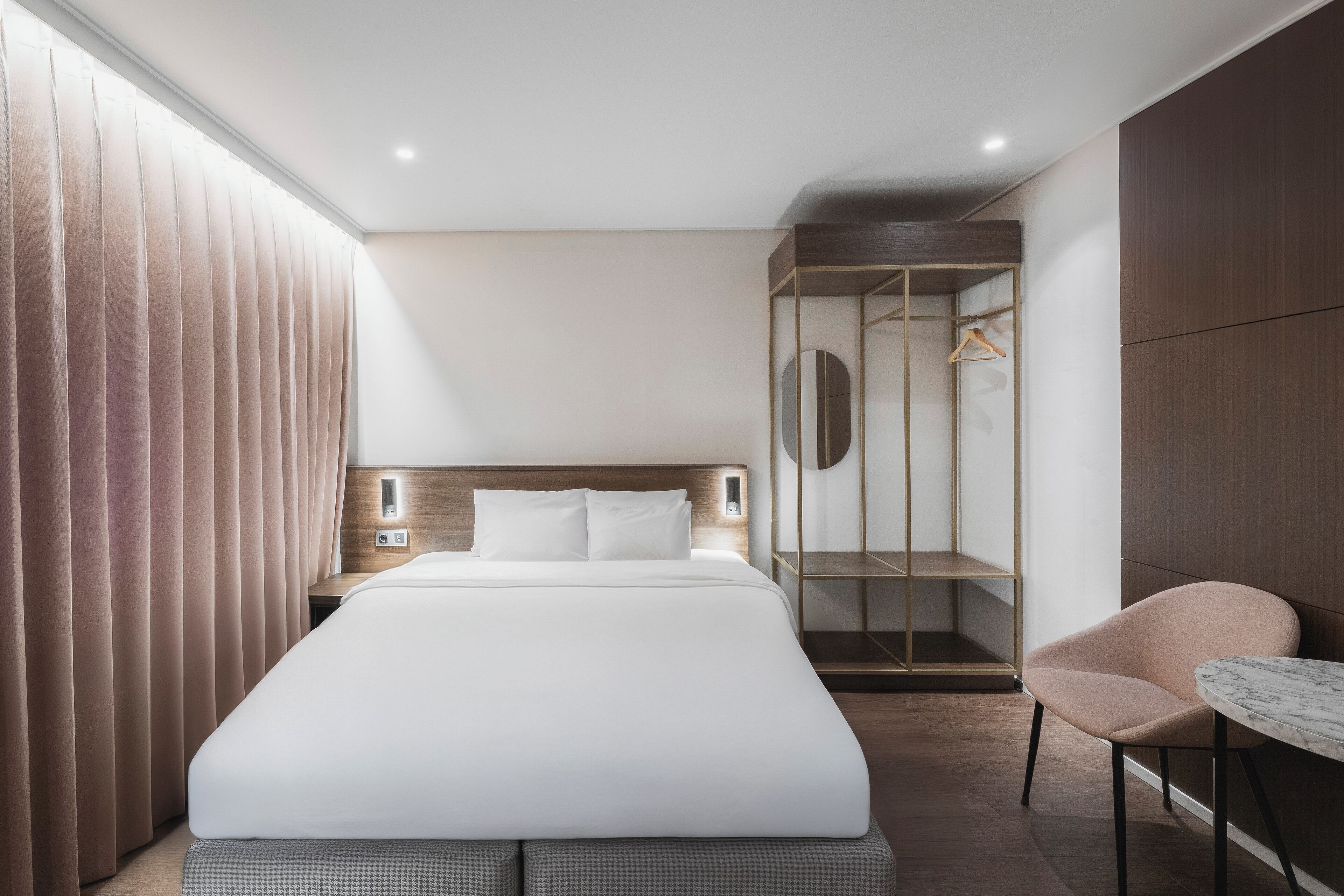 A modern hotel room with a large bed, a seating area with a table, a wardrobe, and a mirror.