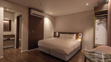 A modern hotel room with a large bed, a marble side table, a wardrobe, and an air conditioning unit.