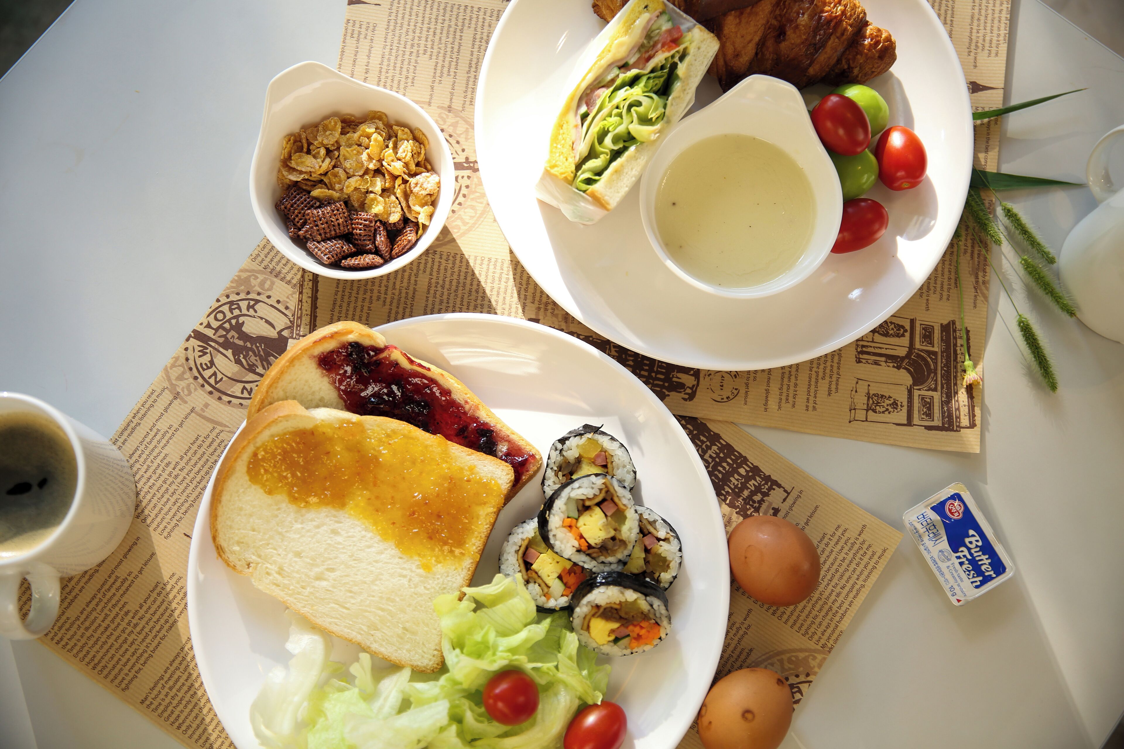 A table with various food items including sandwiches, a bowl of cereal, a cup of soup, and a plate with a slice of toast and a salad.