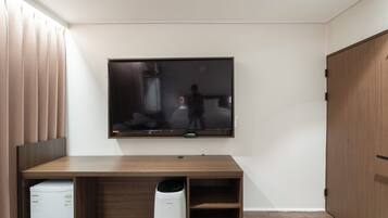 A room with a flat-screen TV mounted on the wall, a wooden desk, a white appliance, and a tall white device on the floor.