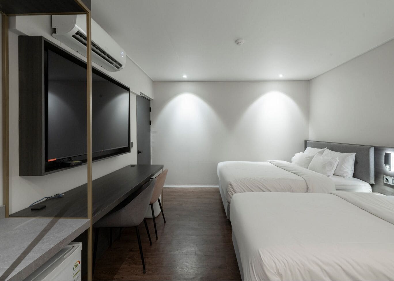 A hotel room with a bed, a desk, a chair, a TV, and a wall-mounted air conditioning unit.
