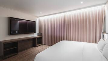 Een moderne hotelkamer met een groot bed, een flatscreen televisie aan de muur, een houten bureau en een groot raam met gordijnen.