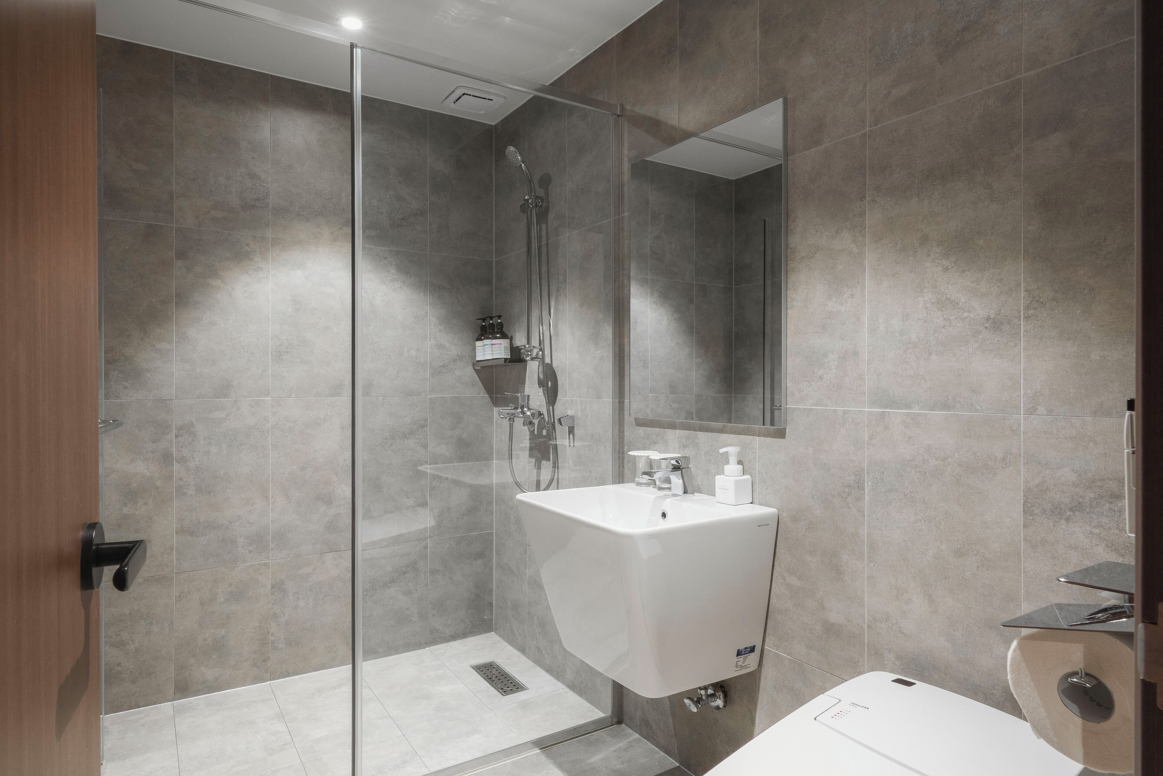 Une salle de bain moderne avec une douche à parois de verre, un lavabo blanc avec un miroir et des toilettes.