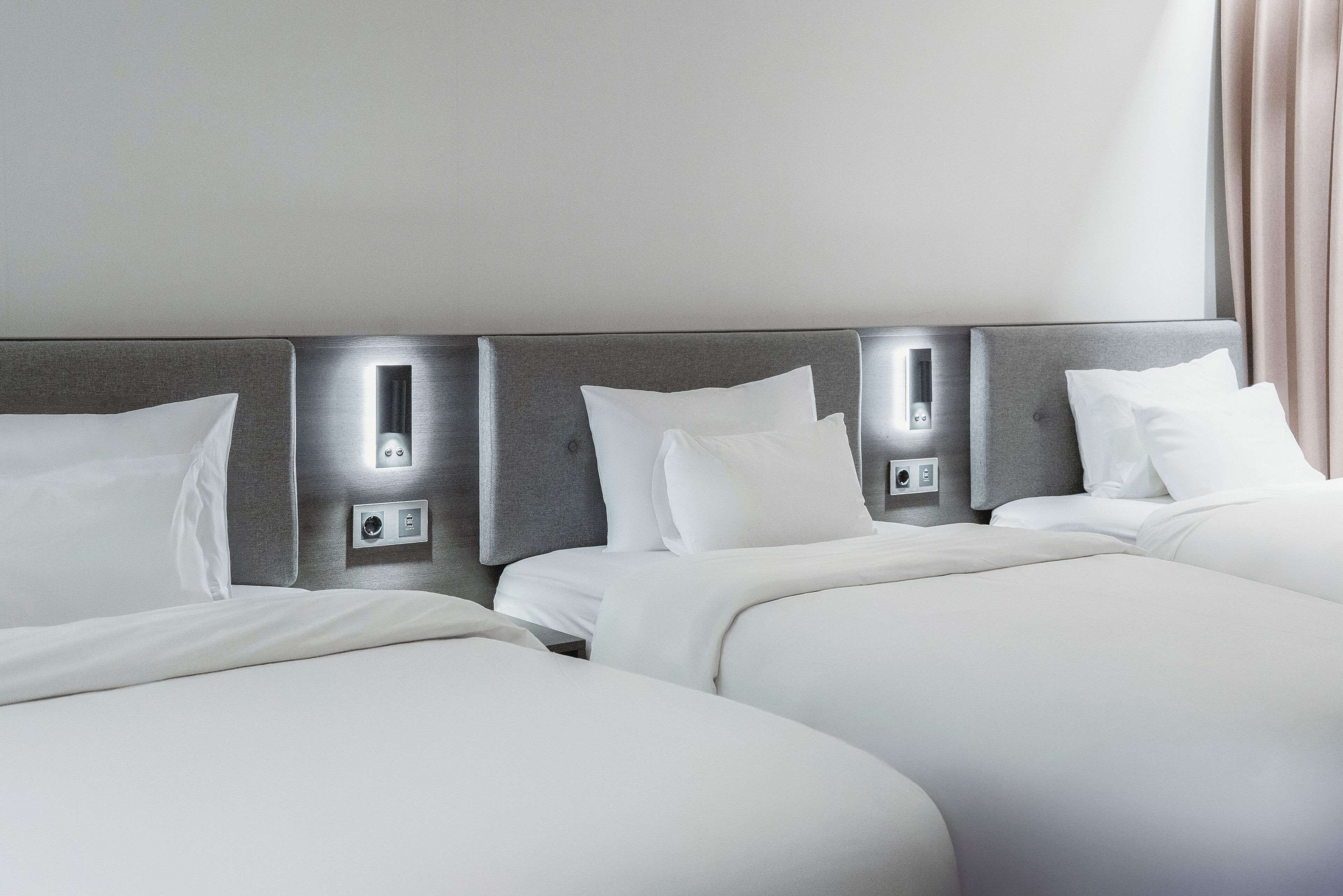 A hotel room with two beds, each with white bedding and headboards with built-in lighting.