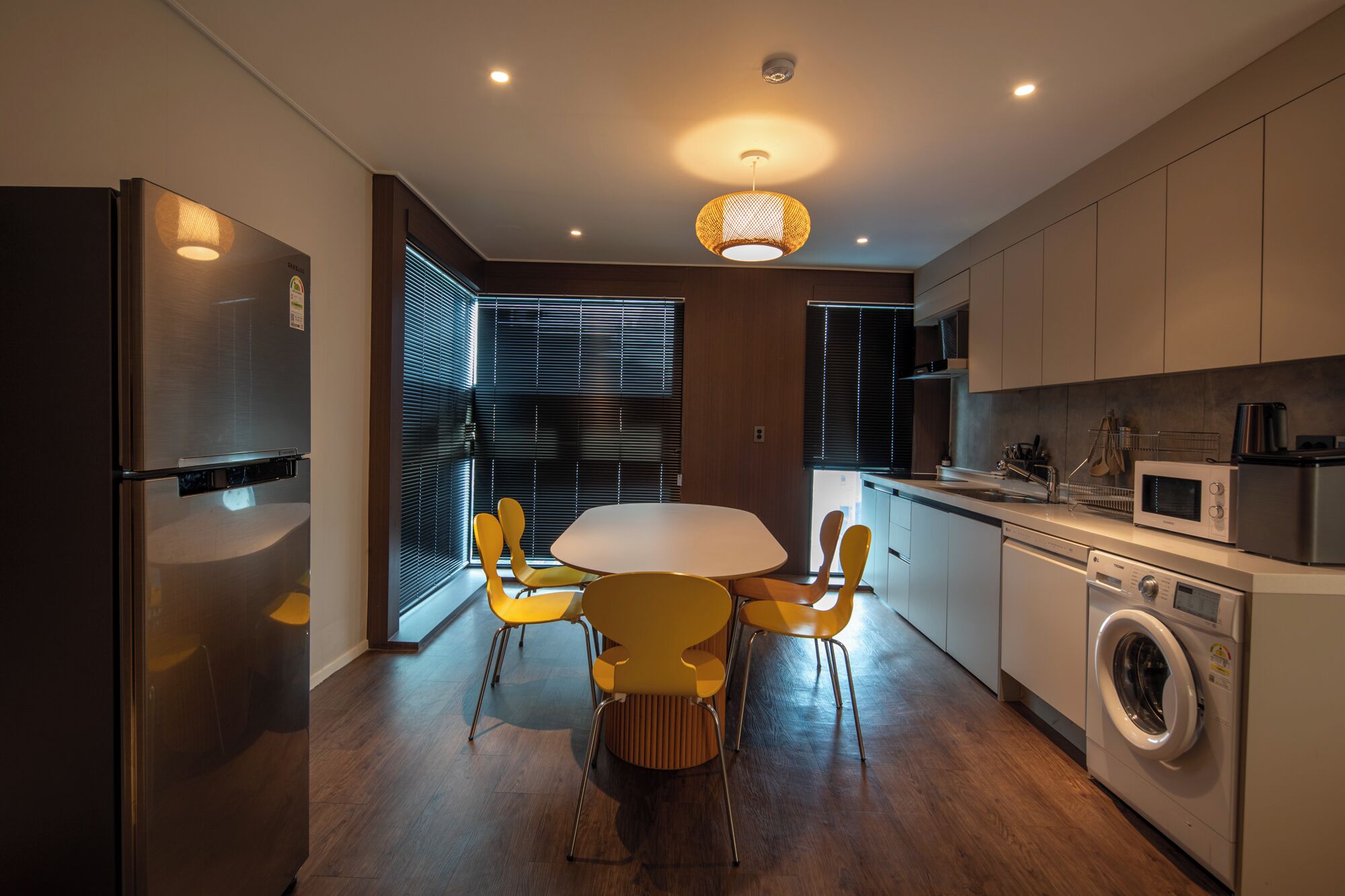 A modern kitchen with a dining area, including a stainless steel refrigerator, a washing machine, and a microwave.