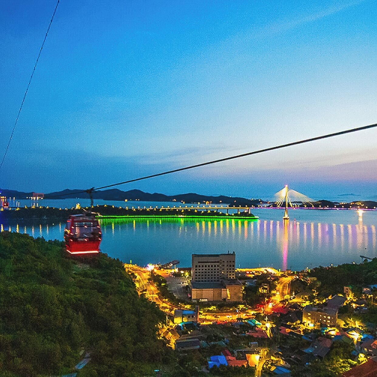 A cable car moving over a body of water with a bridge in the background.