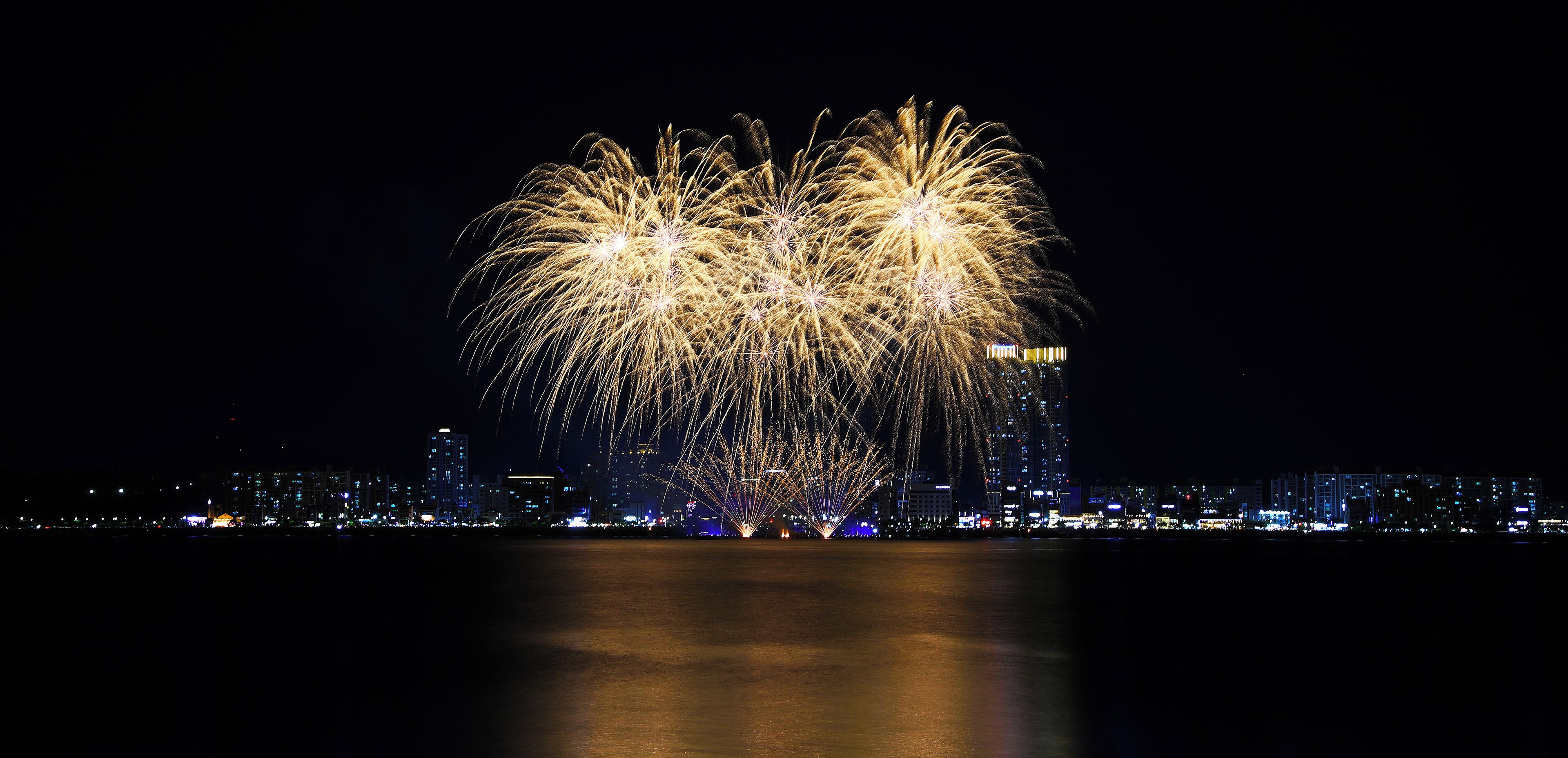 A nighttime cityscape with a large fireworks display over a body of water.