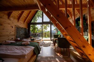 A cozy wooden cabin with a loft bedroom, a dining area, and a large window offering a view of the outdoors.