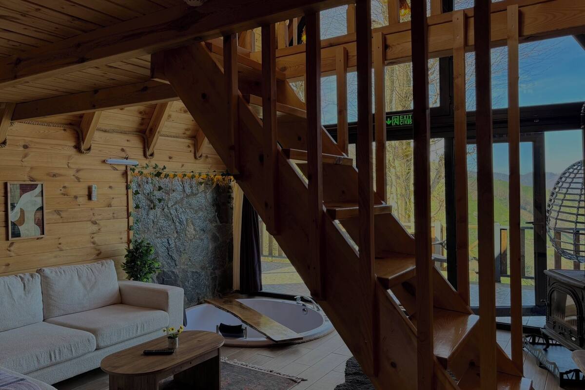 A wooden interior with a sofa, a small table, a stone wall, and a wooden staircase.