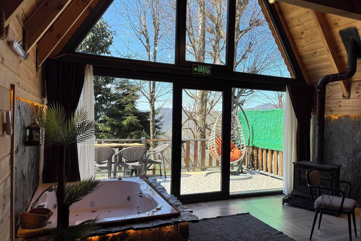 A cozy cabin with a large sliding glass door leading to an outdoor deck, a hot tub, and a stone fireplace.
