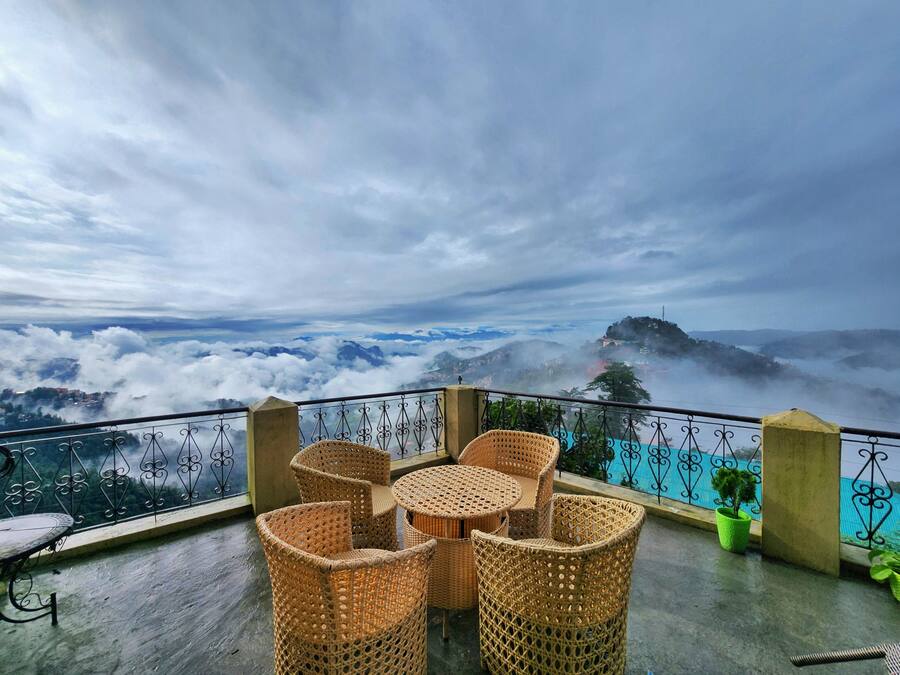 Ein Balkon mit Korbmöbeln und Blick auf Wolken und Berge.