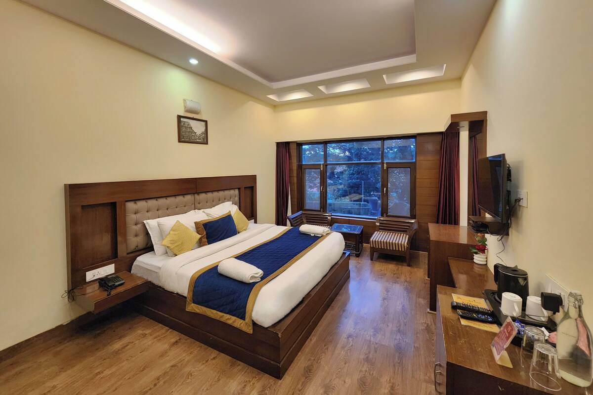 A hotel room with a large bed, a desk with a computer, a TV, and a window with curtains.