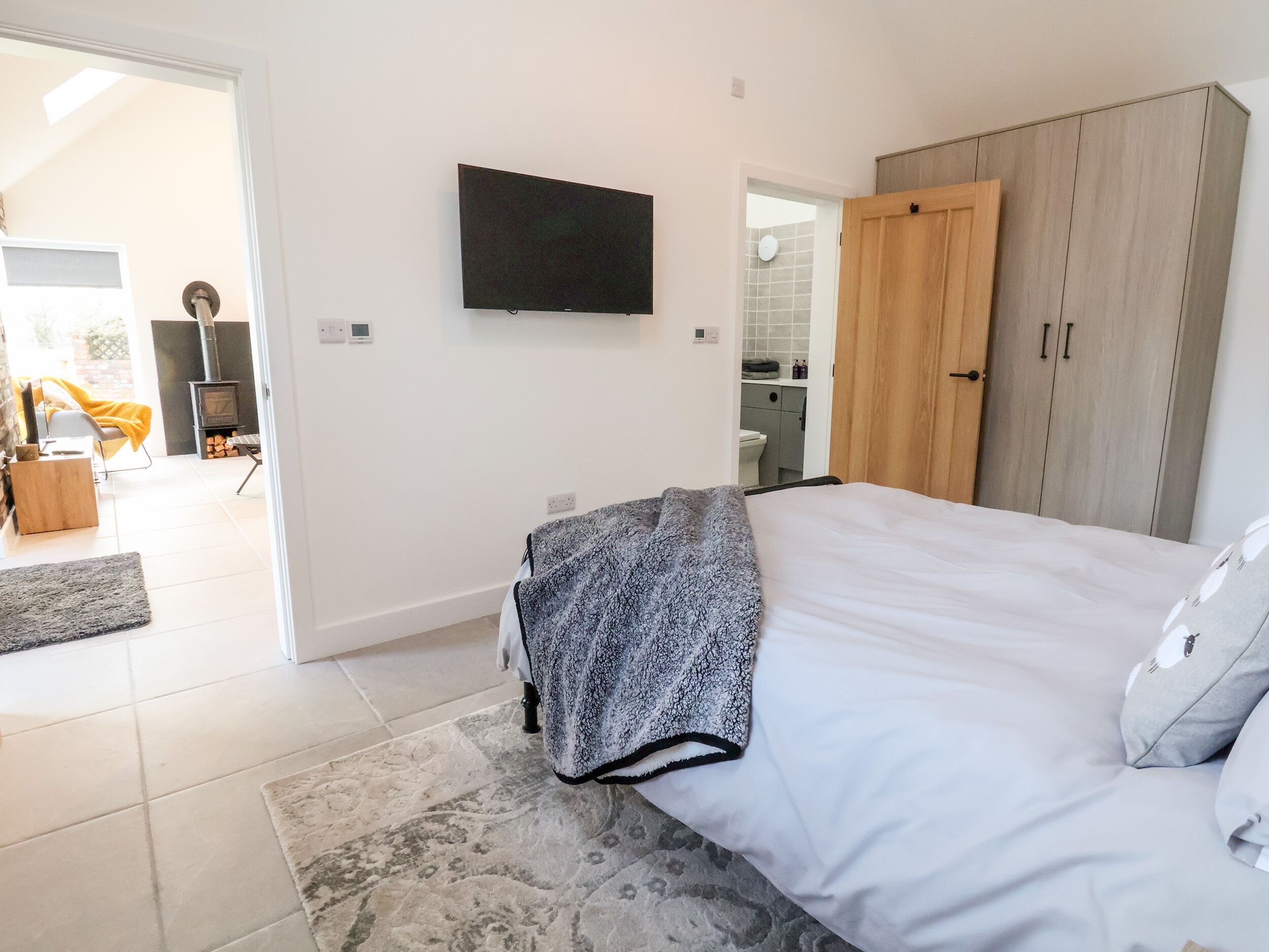 Un dormitorio con cama, televisión montada en la pared, armario y baño visible a través de una puerta abierta.