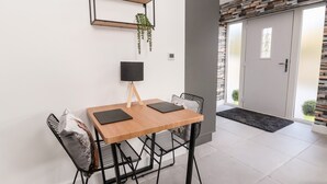 Un comedor con una mesa de madera, sillas negras, una lámpara negra y una planta sobre una estantería.