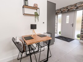 A dining area with a wooden table, black chairs, a black lamp, and a plant on a shelf.