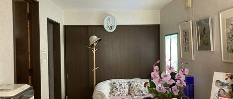 Una habitación con cama, perchero, reloj y una mesa con lámpara.