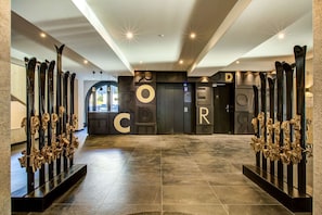 Eine moderne Lobby mit einem zentralen Aufzug, der von skibehafteten Skulpturen und großen Schriftzügen mit dem Wort „EEROR“ gesäumt wird.