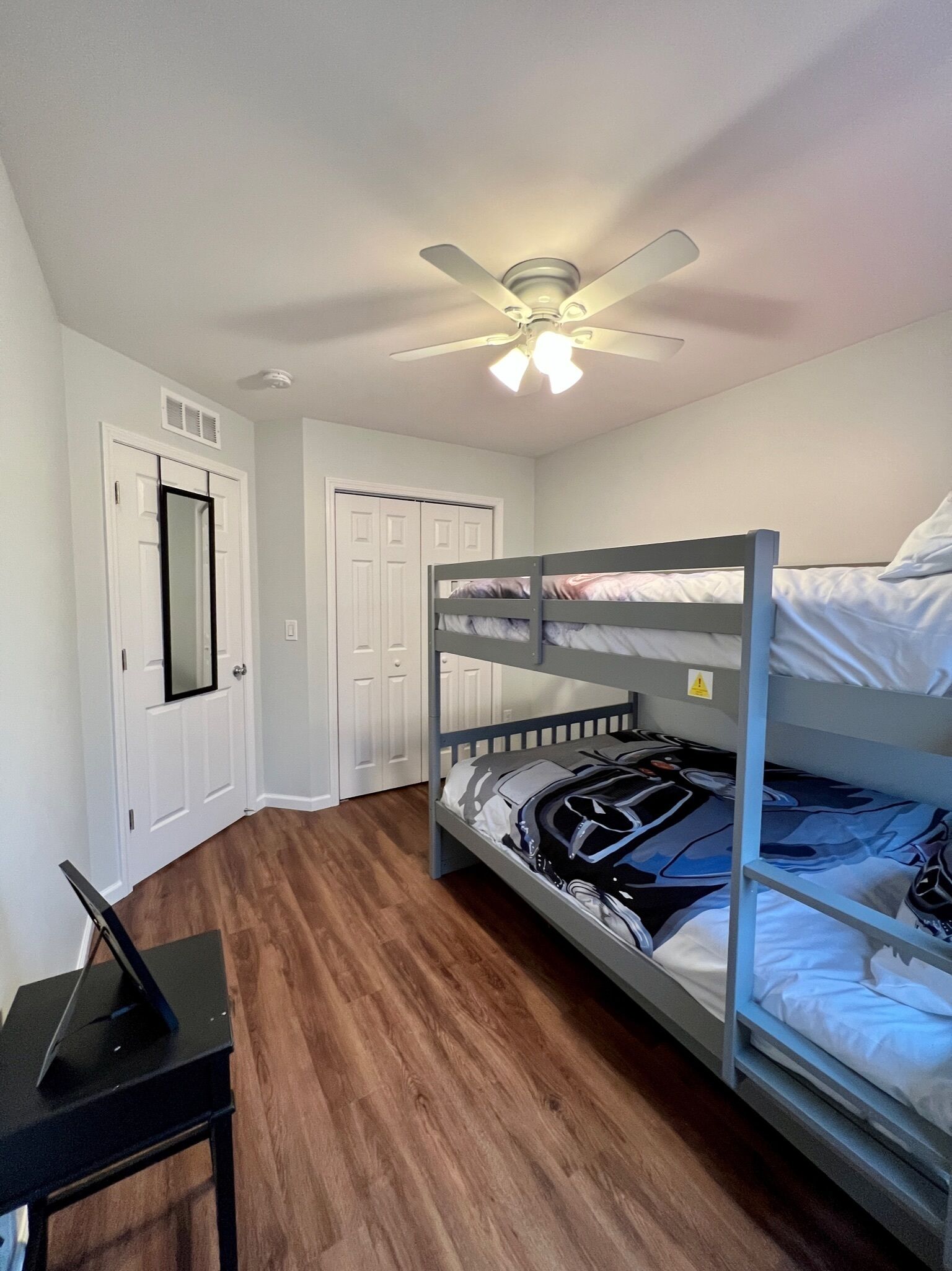 A bedroom with a bunk bed, a desk with a laptop, and a ceiling fan.