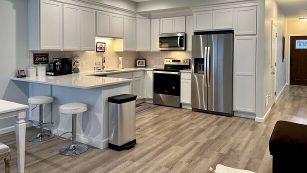 A modern kitchen with white cabinetry, stainless steel appliances, and a central island with bar stools.