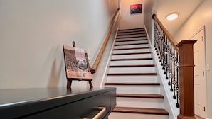 A staircase with wooden steps and a black railing, leading to a landing with a framed picture and a clock.