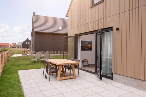 A modern house with a patio, a wooden table, and chairs.