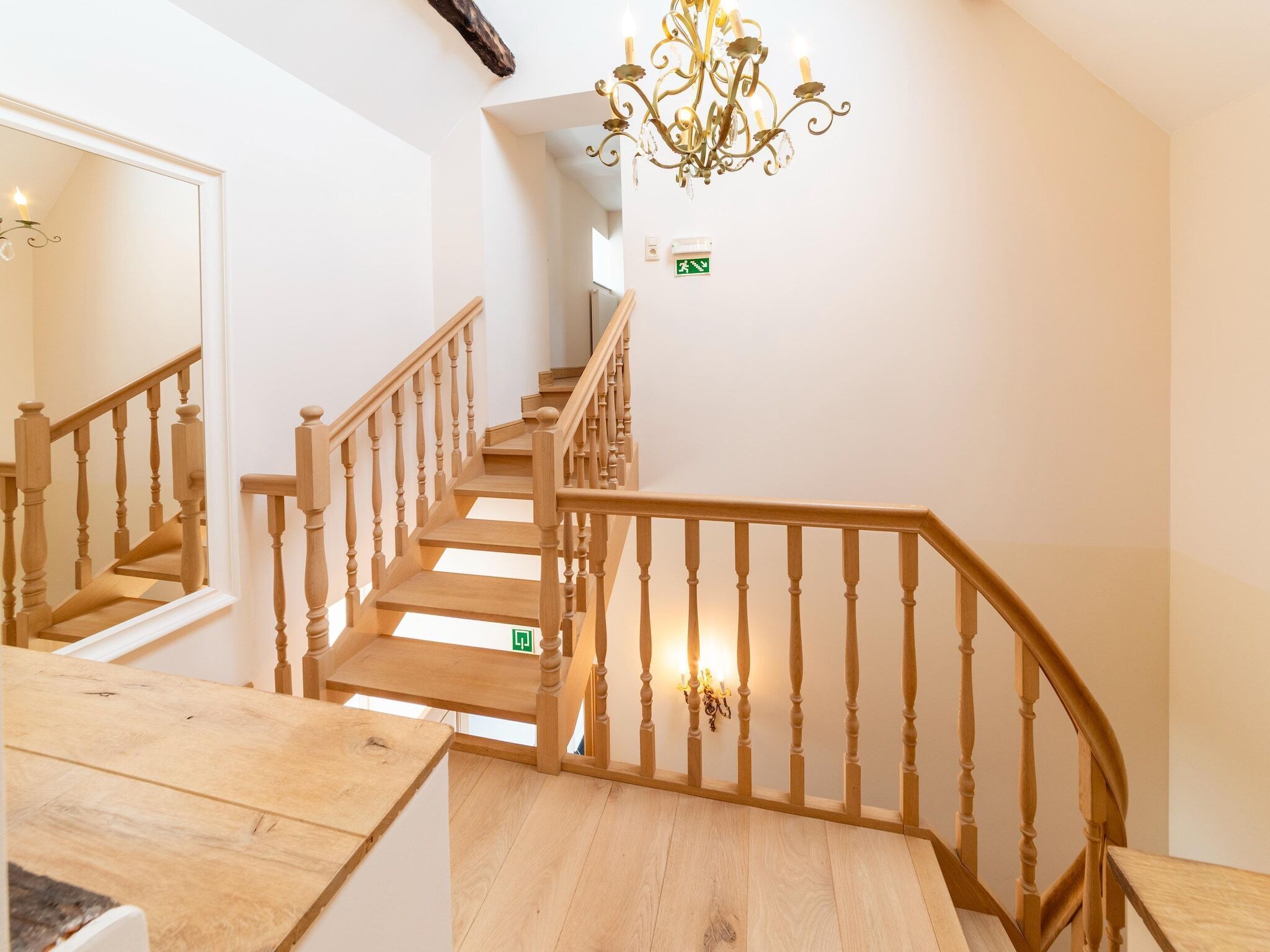 Una escalera de madera con un candelabro, un espejo y una señal de salida verde.