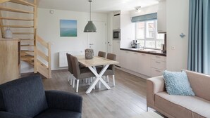 Ein modernes Wohnzimmer mit Treppe, einem Essbereich mit Holztisch und Stühlen, einer Küche mit Fenster und einer Couch mit Kissen.