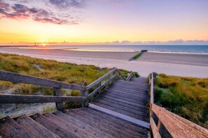 A wooden boardwalk leading to a beach with a sunset in the background.