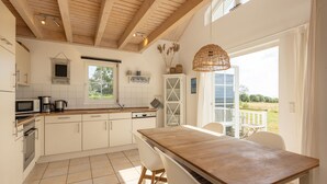 A modern kitchen with white cabinets, a wooden dining table, and a view of the outdoors. - Bungalow by the Sea with Sauna in Germany (Sierksdorf)