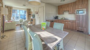A modern kitchen with wooden cabinets, a dining table with chairs, and a large window providing natural light.