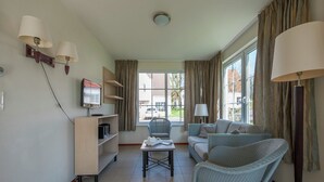 A modern living room with a sofa, armchair, and a small table. There is a television on a stand and a bookshelf. - Quiet Villa in Lower Saxony (Bad Bentheim)