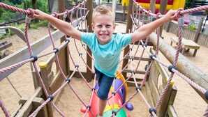 A child on a rope bridge at an outdoor playground with a slide and picnic tables in the background. - Villa with bubble bath, solarium and fireplace (Dahlem)