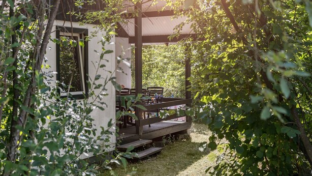 Eine Holzhütte mit überdachter Veranda, umgeben von üppigem Grün.
