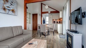 A modern living room with a sofa, coffee table, and a fireplace. There is a dining area with chairs and a kitchen in the background.
