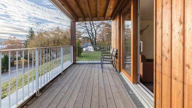 A wooden balcony with a view of a road and trees, a bench, and a sliding glass door leading to an interior space. - Winterberg Stay with Beautiful View (Winterberg)